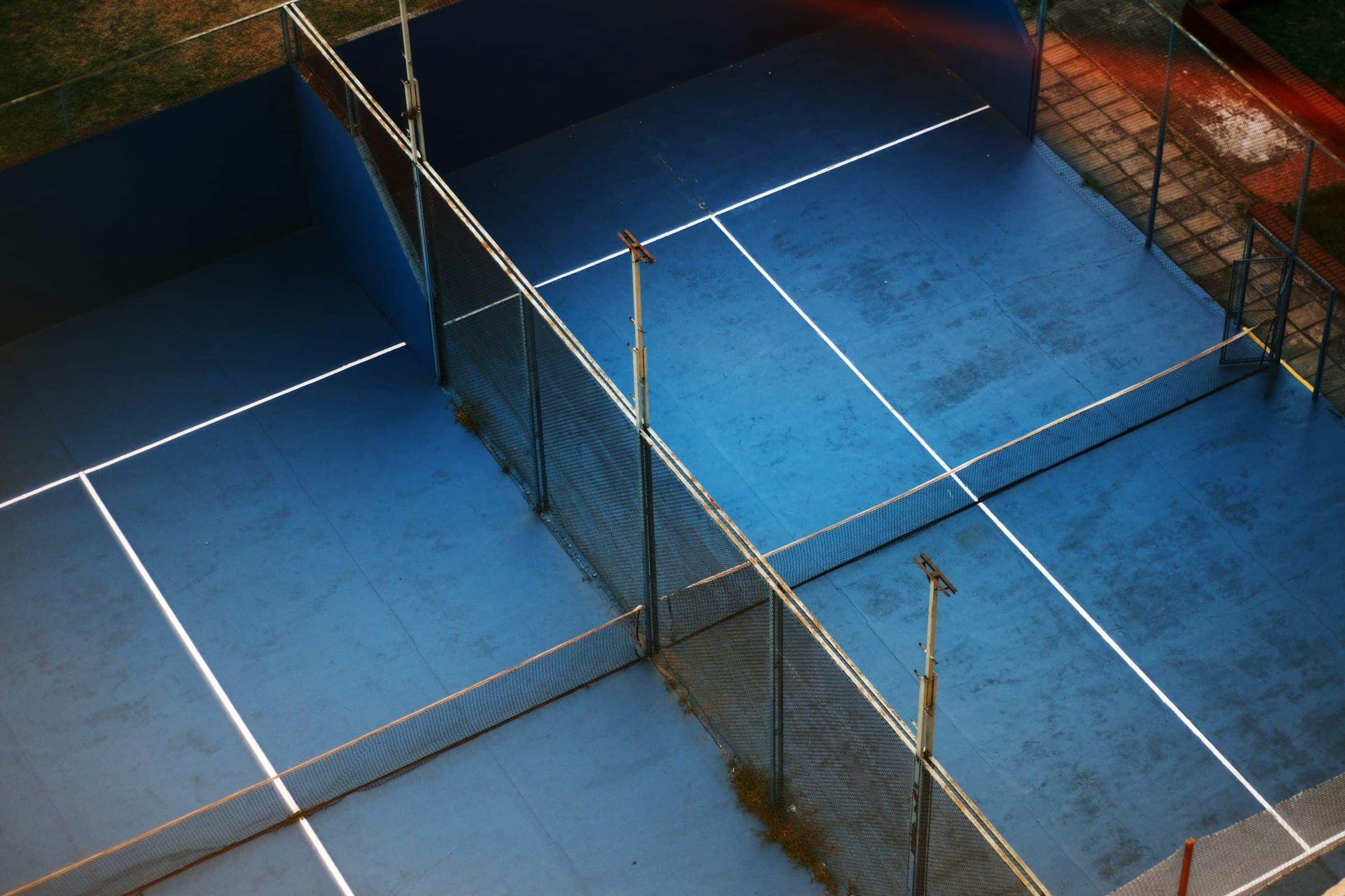 Aerial view of a blue padel court with its net and glass walls