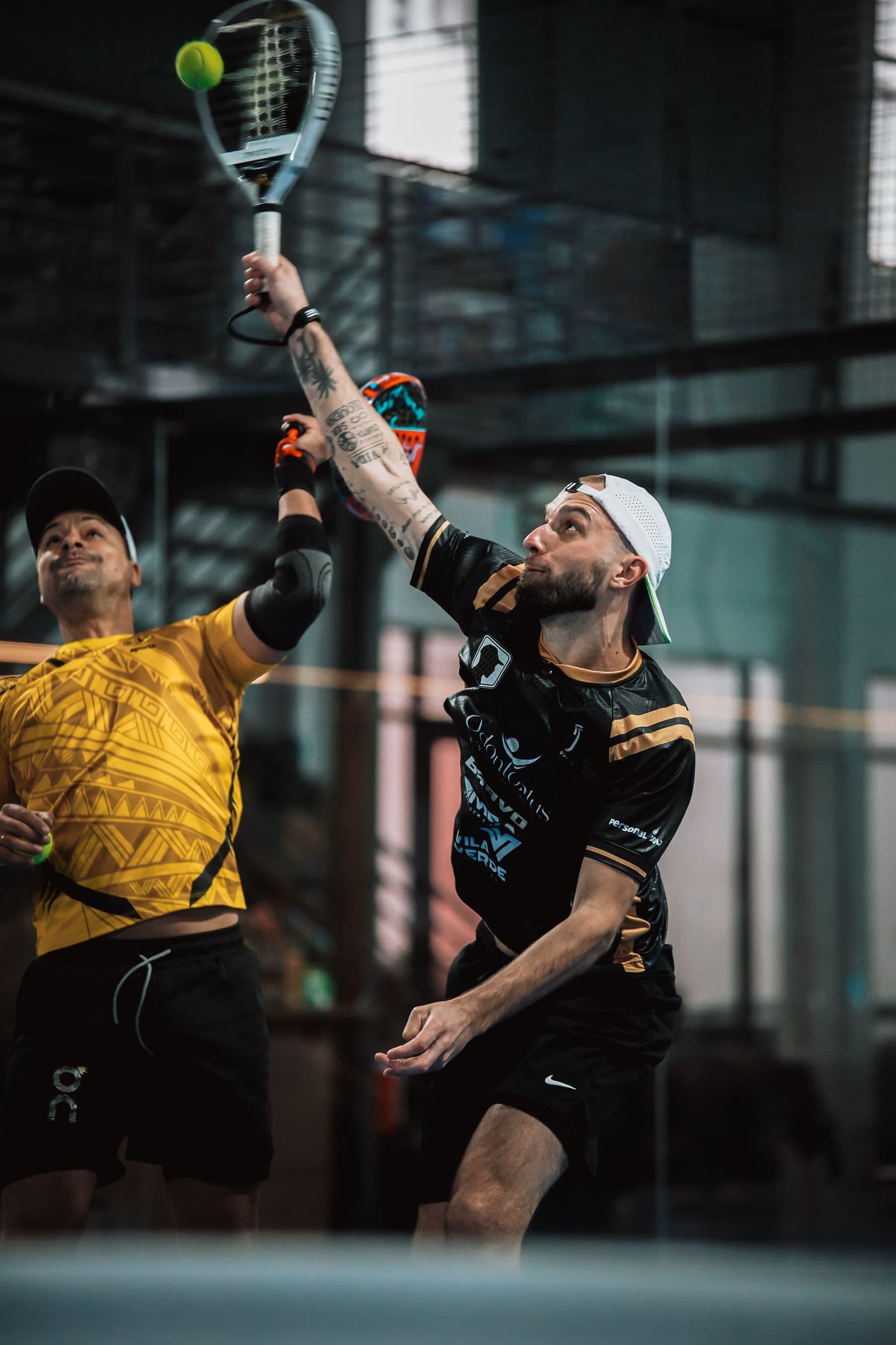A doubles player hitting an overhead while their partner watches