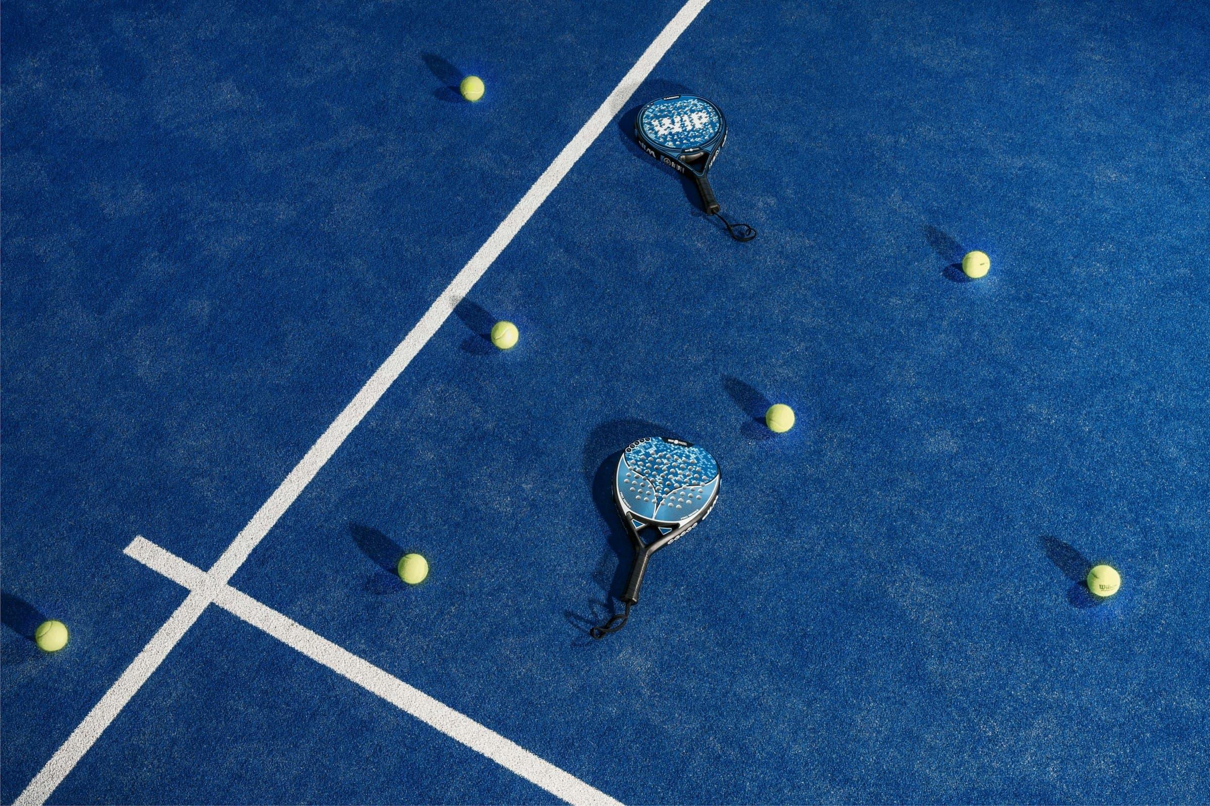 Two padel rackets and scattered balls on a blue court, seen from above
